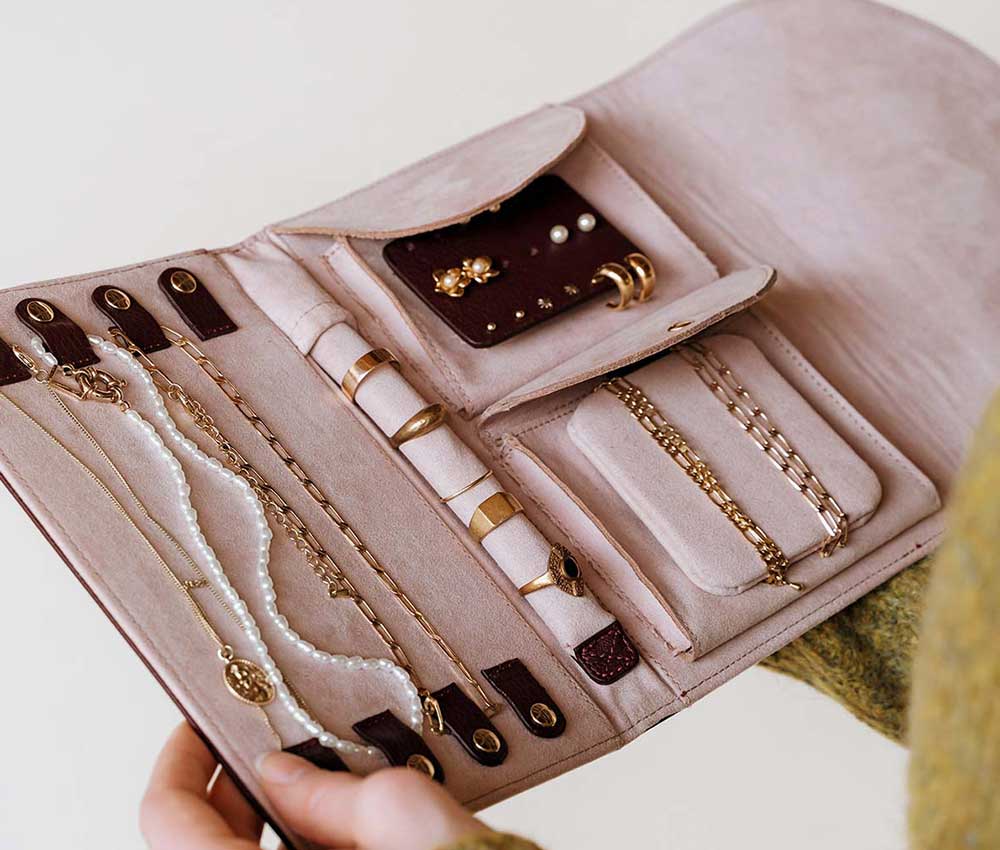 An open pink and burgundy leather jewellery case filled with gold jewellery from Poppy Barley.
