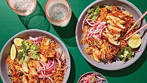 Two bowls of curry-coconut sheet pan noodles with chicken and kale, served with onions and cilantro