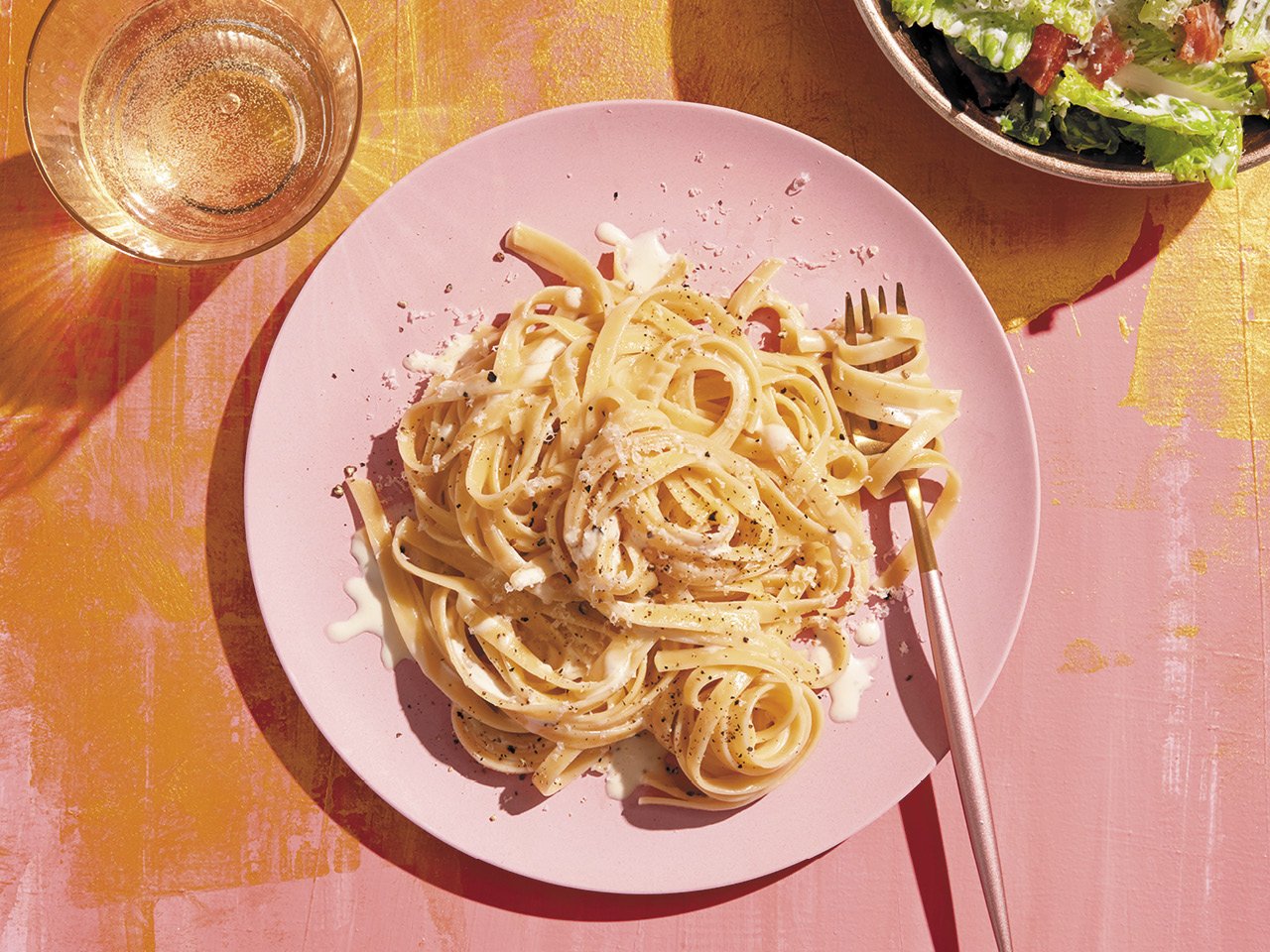 Prosecco fettuccine alfredo served on a plate alongside sparkling wine and a salad