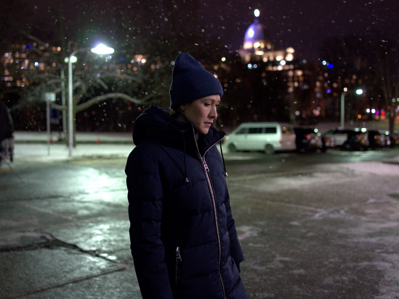 A woman in a dark jacket and toque walking across the street.