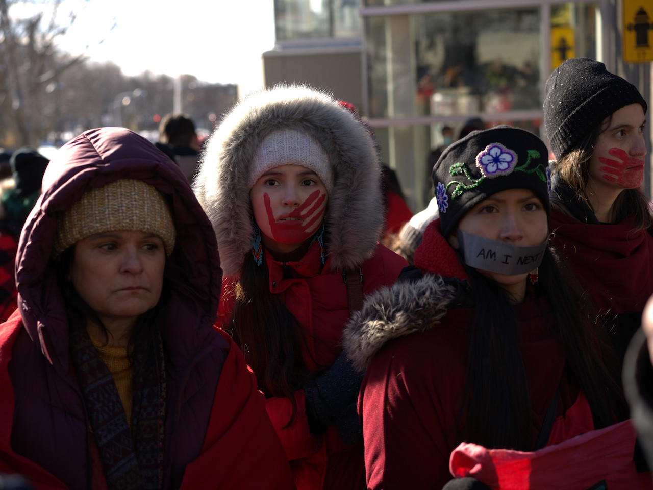 Three women in red parkas at a MMIWG protest.