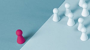 Conceptual art featuring a bunch of white chess pieces grouped together and one pink piece all alone.