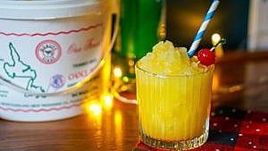 recipe of a glass of yellow pineapple slush with a cherry and paper straw for Christmas