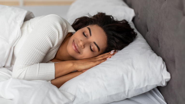 A woman sleeping on her side in a bed with a smile on her face.