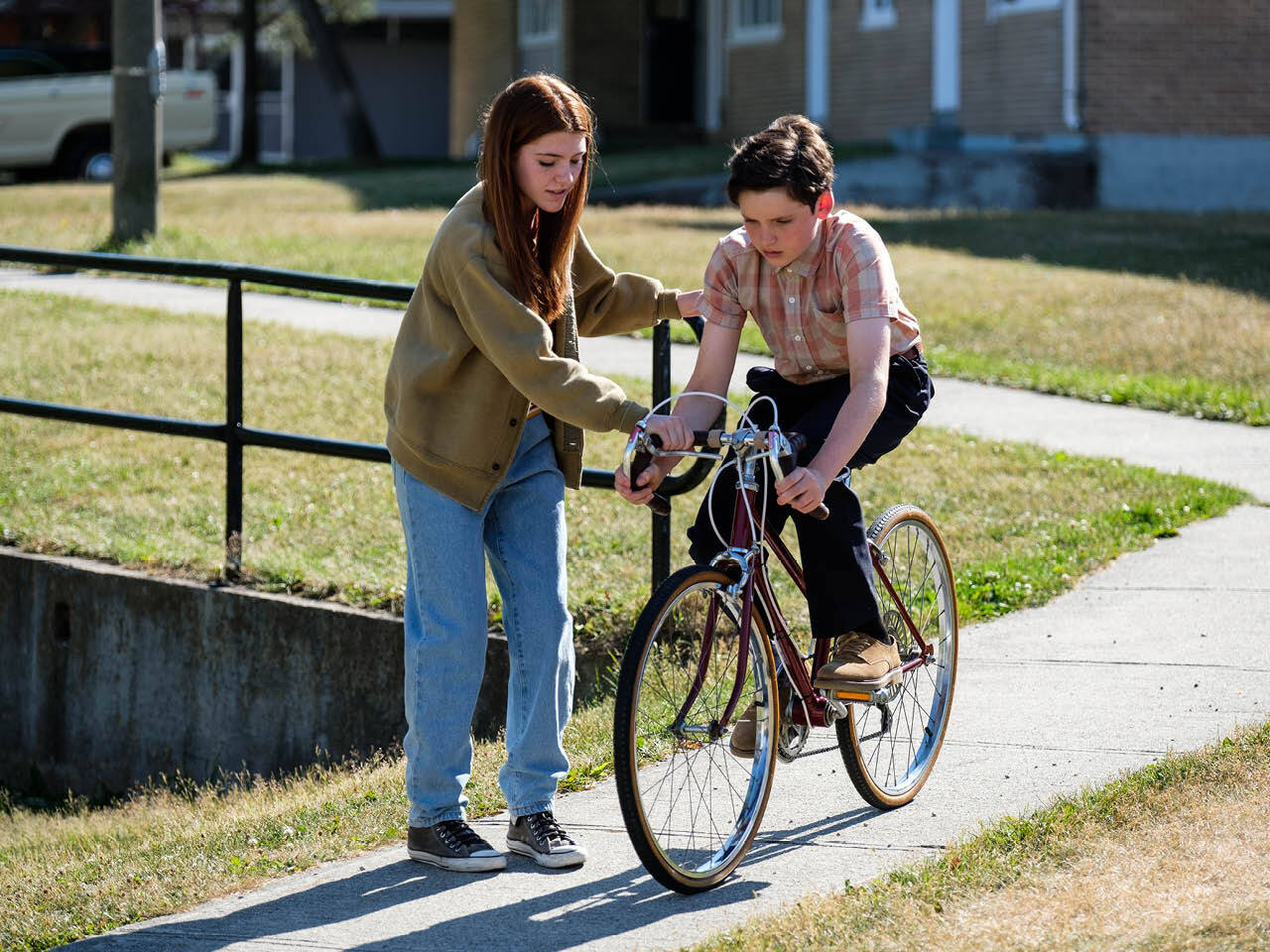 A tweenage girl helps a younger looking boy learn to ride a bike.