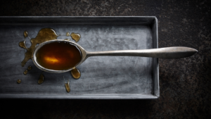 A spoonful of maple syrup sits on an aluminum tray on a dark countertop
