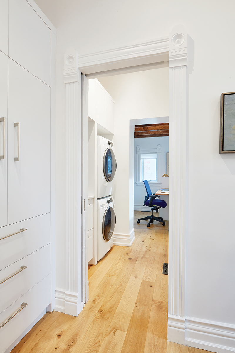 White cabinets leading to an open doorway that opens onto a stacked washer and dryer and then another door with a desk chair in front of a window