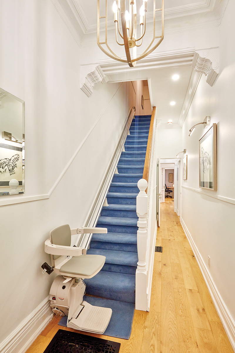 The staircase in the front hall with a stair lift and a blue runner carpet