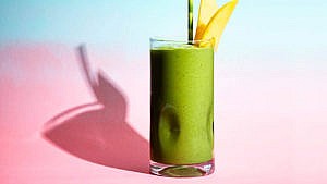 A green smoothie with a green straw, garnished with two mango spears