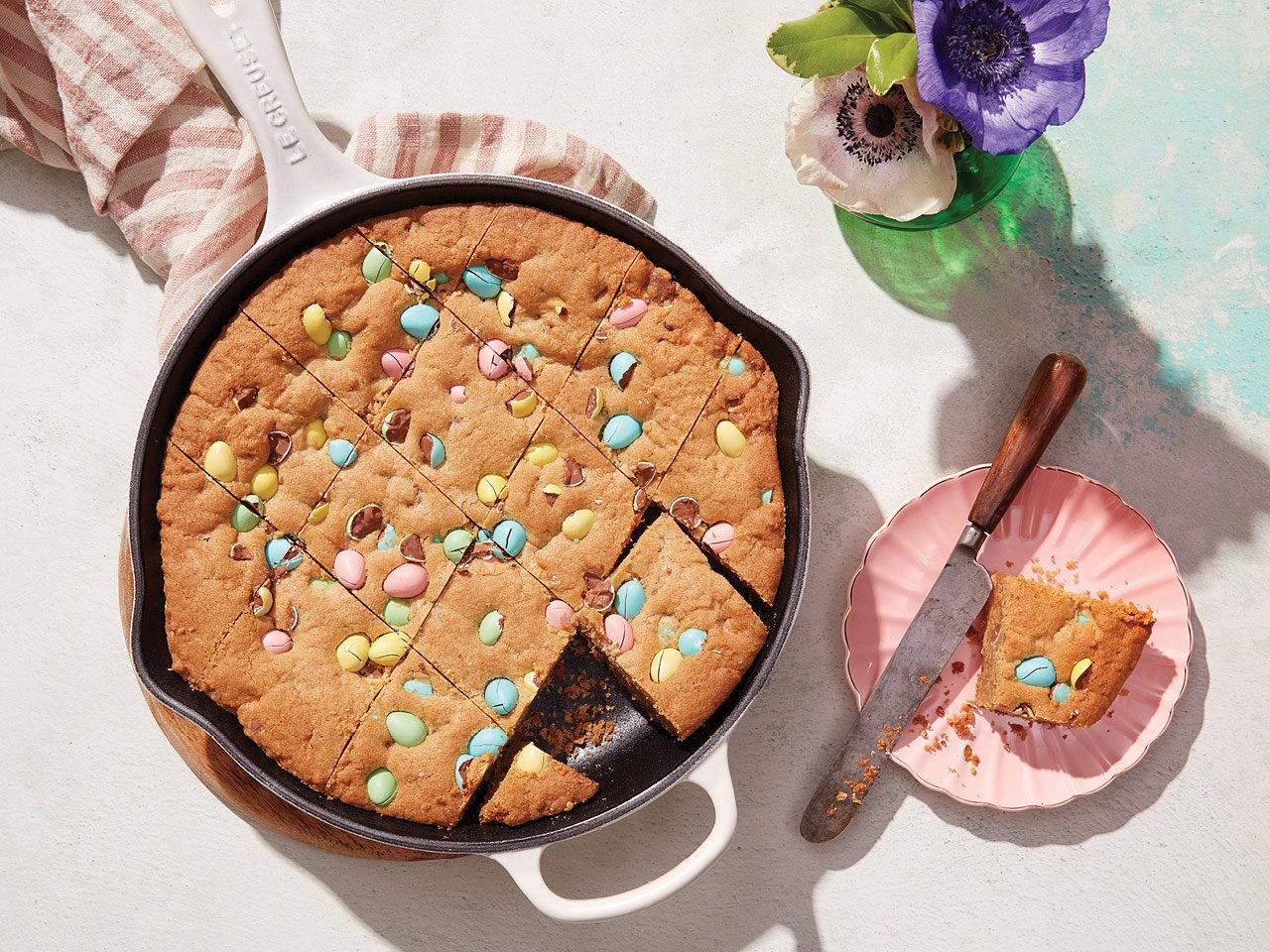 a skillet cookie in a pink cast iron pan cut into squares. a piece is taken out