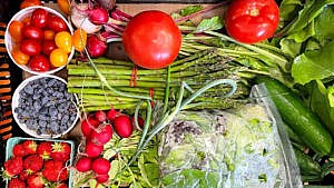 The interior of a market farm box, with asparagus, tomatoes, salad leaves, berries and more