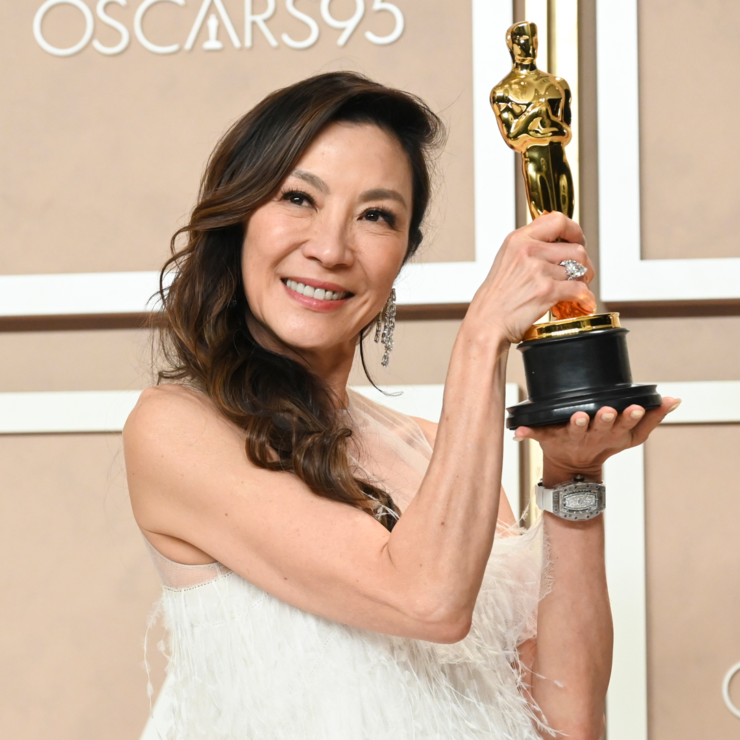 A woman in a feathery white dress holds an Oscars statuette