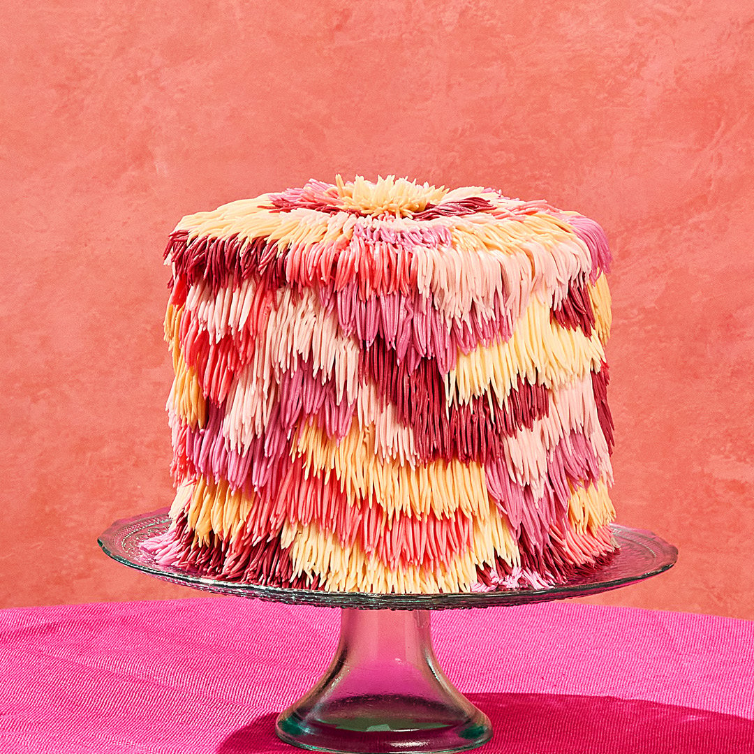 A photo of a very tall layer cake with shaggy, multicoloured icing.