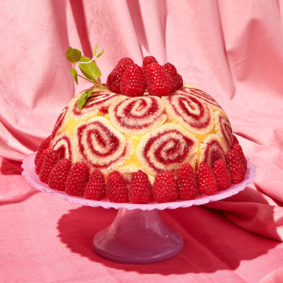 A domed cake with an outer layer of jelly cake rounds, and raspberry garnish.