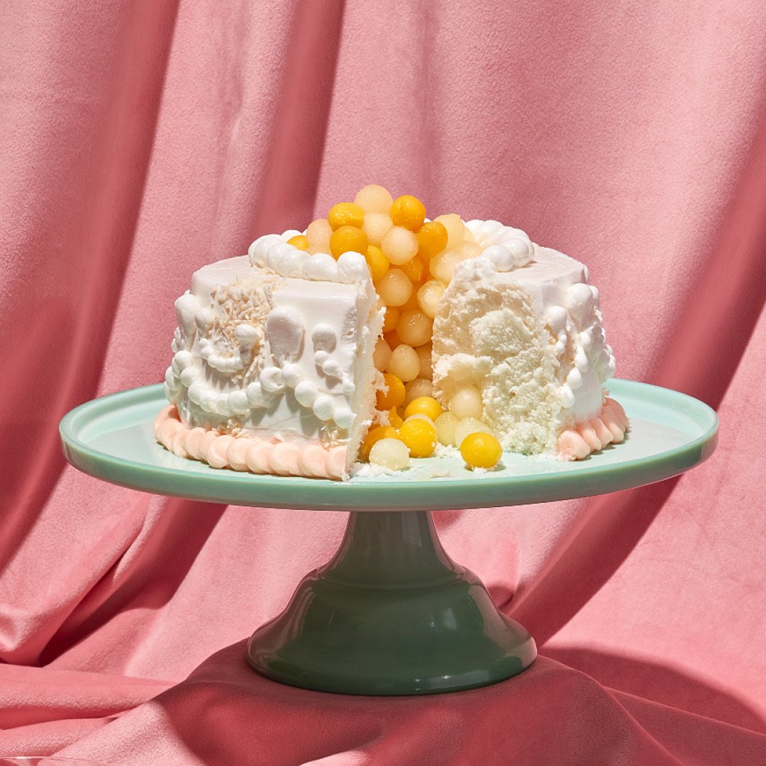 A photo of a white frosted ring cake with orange balled fruit in the middle.