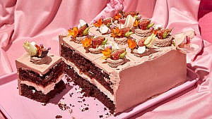 A decadent nanaimo cake topped with floral adornments, with one slice cut ready to serve