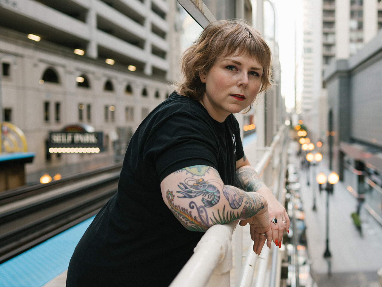 Author Tracey Lindeman leans against a railing in a city, looking at the camera. Lindeman suffered with endometriosis for decades before having a hystectomy.