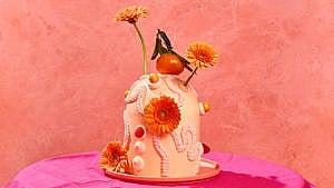 Orange cream cake topped with orange buttercream icing, oranges, and orange daisies