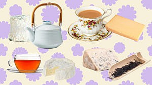 Various cheeses and cups of tea in front of a light background with solid purple flowers.