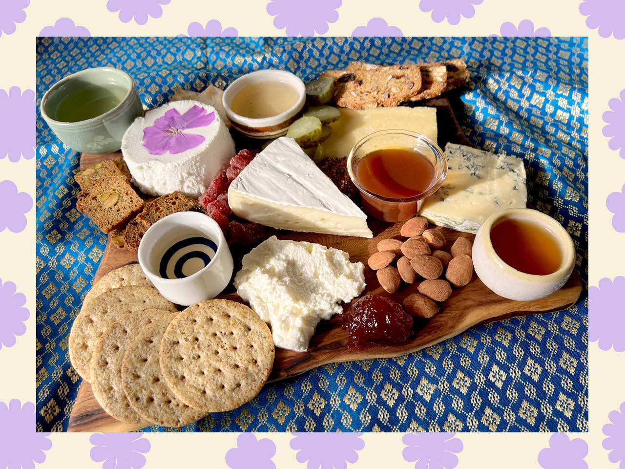 A cheeseboard with various nuts, crackers, cheese and cups of tea.