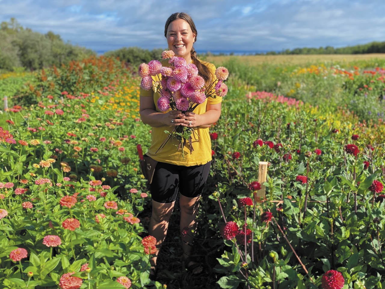 A woman standing in a field of flowers holding a bouquet of pink flowers