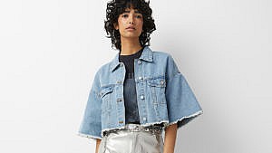 A model seen from the waist up wearing a cropped, short-sleeved denim jacket.