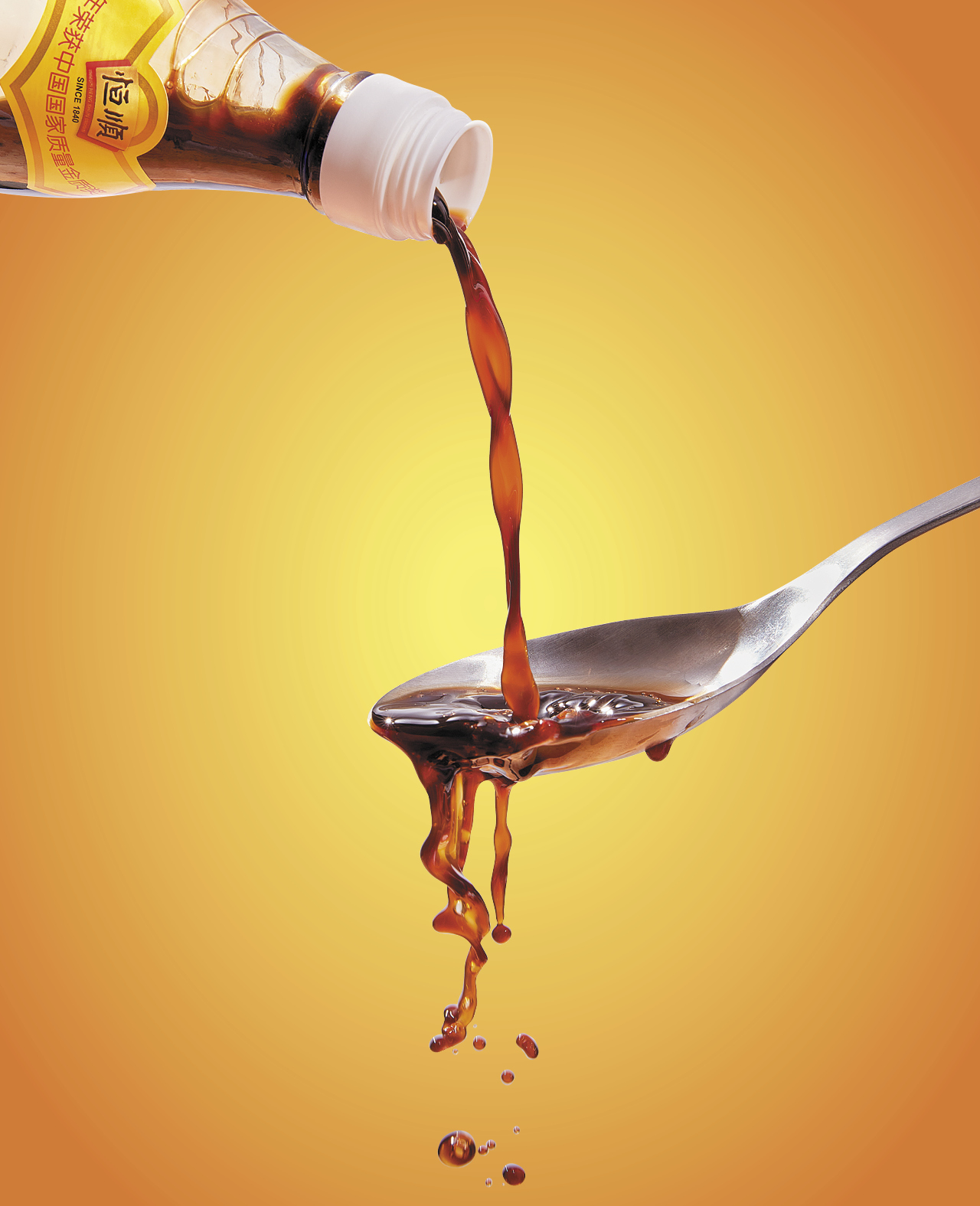 A spoon with black vinegar being poured into it and splashing over the sides with a yellow background