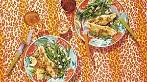 Two plates of lemon butter haddock with capers on a leopard-print tablecloth with a side of green beans