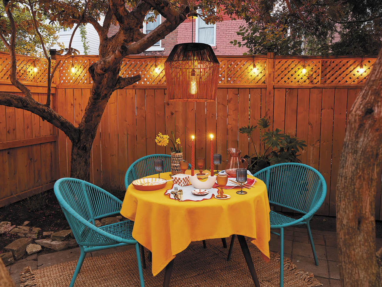 A table set outdoors in a backyard with a solar-powered outdoor pendant light hanging above from a tree.