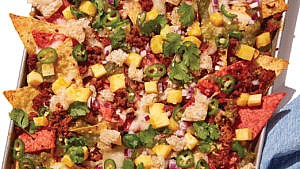 Chorizo and pineapple nachos served on a tray with cilantro and sliced jalapeno
