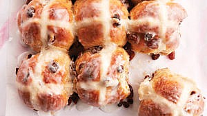 a tray of hot cross buns with raisins on parchment paper, with one pulled off and ready to be eaten