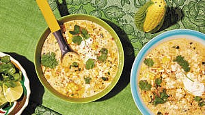 A bowl of elote chowder served alongside other dishes on a green tablecloth