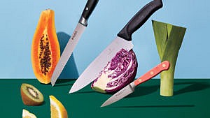 three knifes sit point-down in a piece of papaya, red cabbage, and a leek