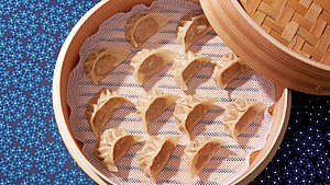 Jiaozi (or Chinese dumplings) laid out in a wooden steaming basket to be cooked as potstickers