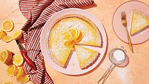 Classic lemon tart decorated with sugar icing on a pink plate.