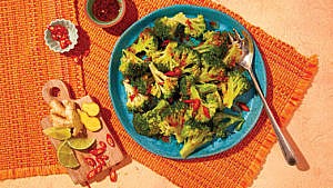 Brocoli decorated with asian dressing and diced red chilli on a blue plate.