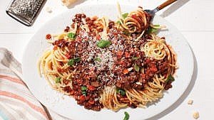Lentil Bolognese with parmesan and chopped basil on top, on a white plate.