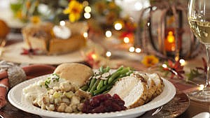 A white plate filled with a traditional turkey dinner including stuffing beans, a dinner roll and cranberry sauce.