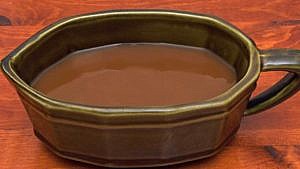 An olive green gravy boat filled with gravy.