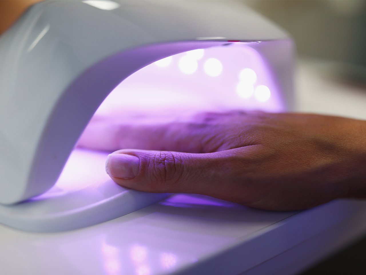 A hand in a UV curing lamp for an article on whether gel manicures are dangerous.