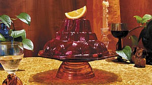 A tall Cointreau Cranberry Jelly topped with an orange wedge, served on a cake dish