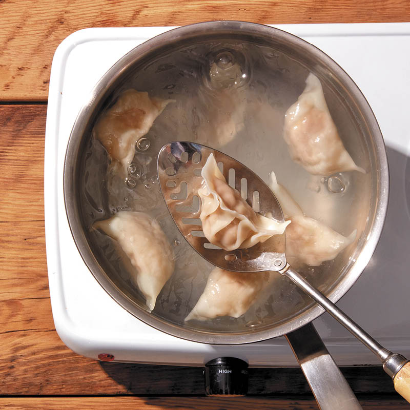 Boiled dumplings: Jiaozi being lowered into a pot of boiling water with a slotted metal spoon