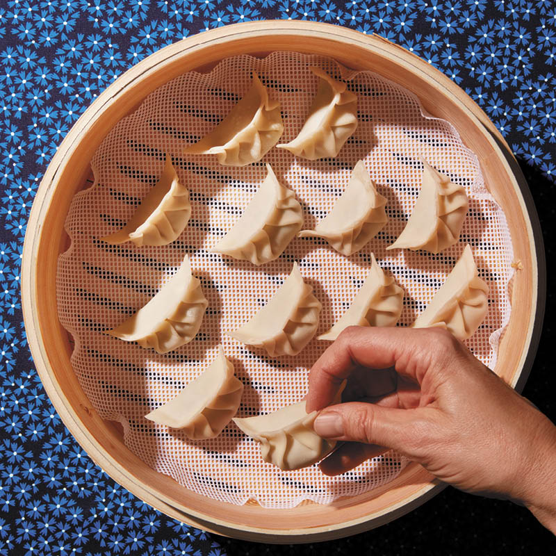 Steamed dumplings: A person adding jiaozi to a bamboo steamer by hand