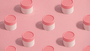 White skincare jars with a pink cap repeated on a pink background.
