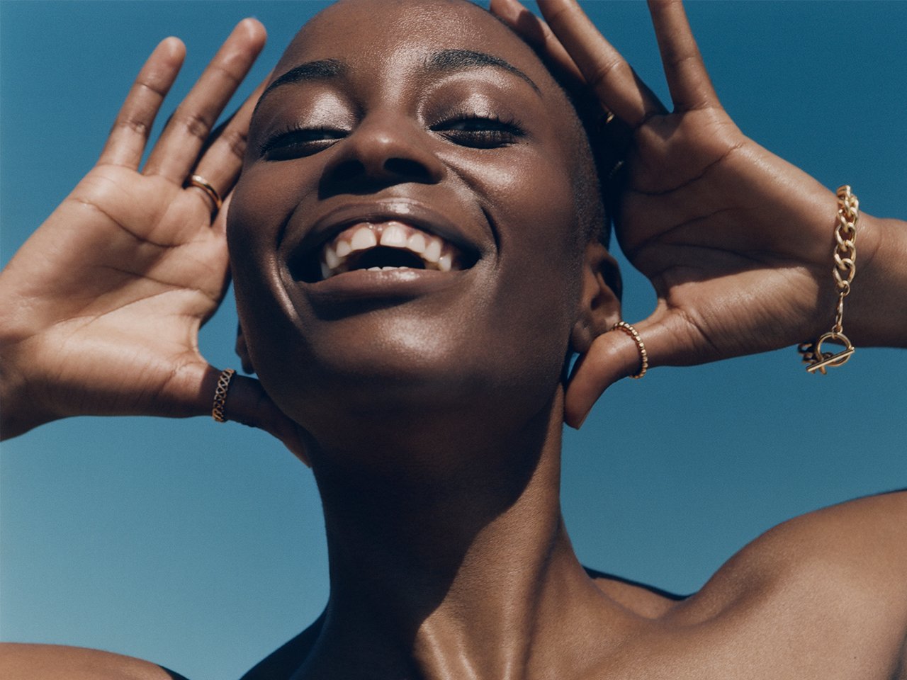 A model with glowing skin photographed smiling in the sun to illustrate an article about vitamin C in skincare.