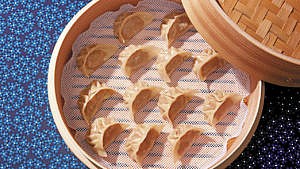 Jiaozi (or Chinese dumplings) laid out in a wooden steaming basket to be cooked as potstickers