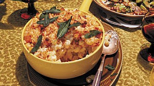 A large bowl of macaroni and cheese with butternut squash topped with crispy sage served as a part of a Thanksgiving spread