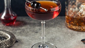 manhattan cocktail garnished with sweet maraschino cherries on a grey-stone counter.