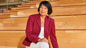 Mayor Olivia Chow at the Canadian Opera Company’s Four Seasons Centre for the Performing Arts in Toronto. She sits on wooden steps wearing a red blazer and white pants.