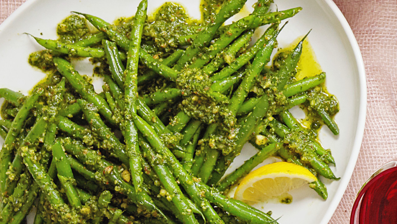 A white platter of green beans dressed with pesto.